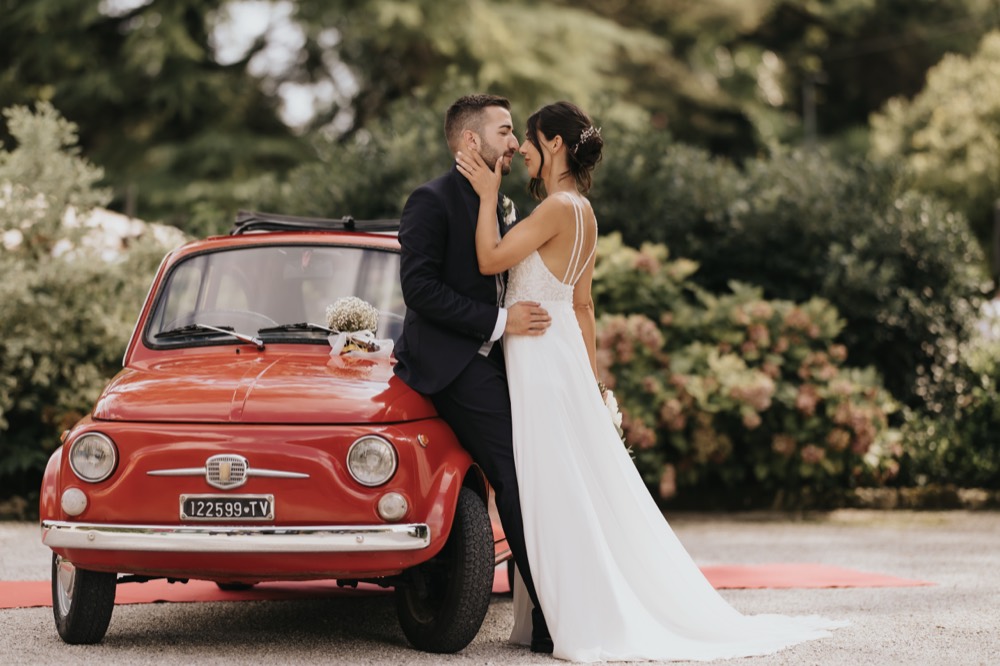 The couple embracing next to a red Fiat 500