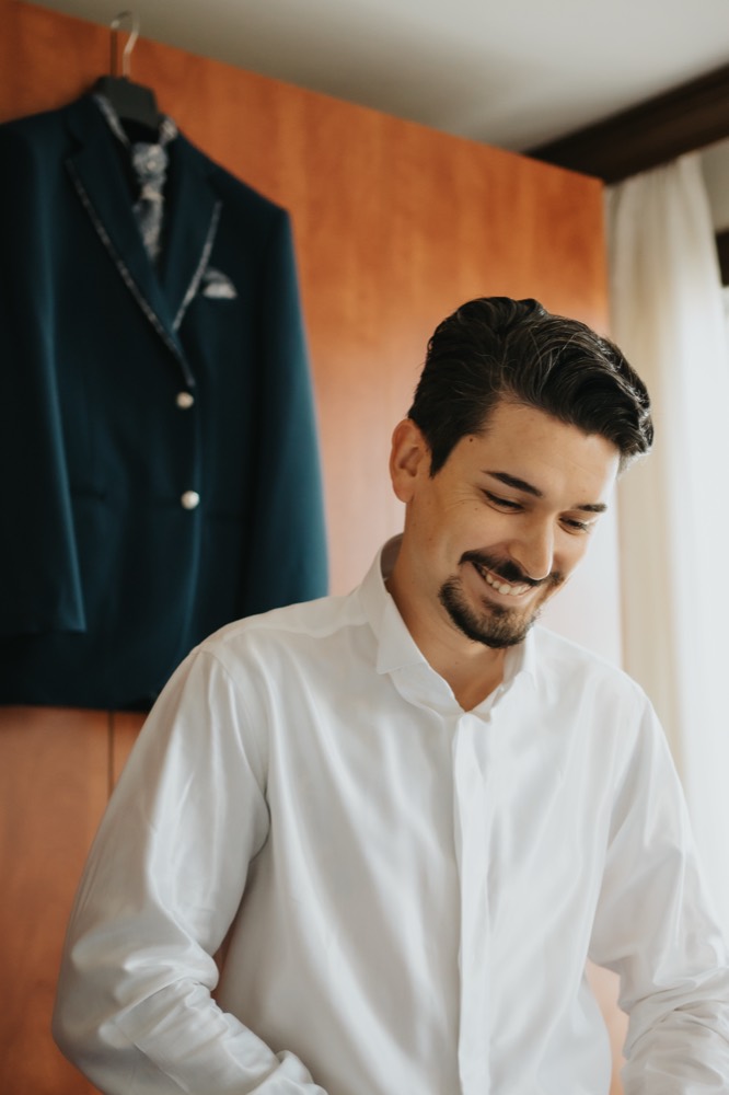 Lo sposo sorride mentre si abbottona la camicia